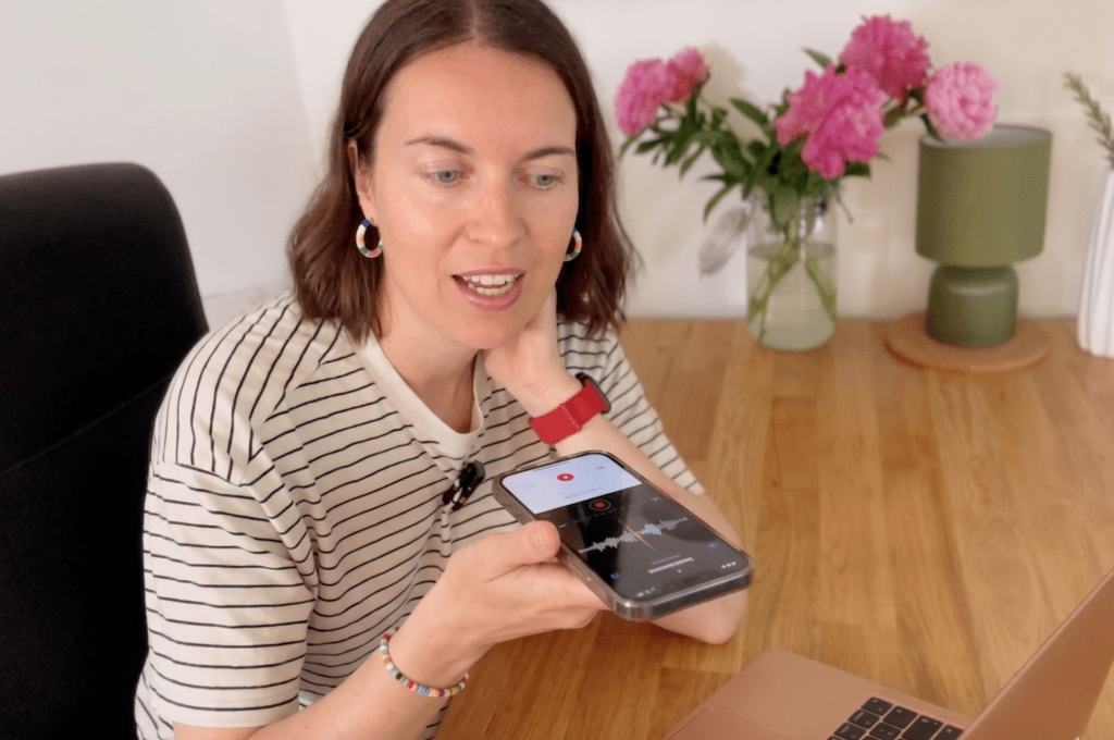 a woman sitting at a desk, holding a phone and recording a voice message